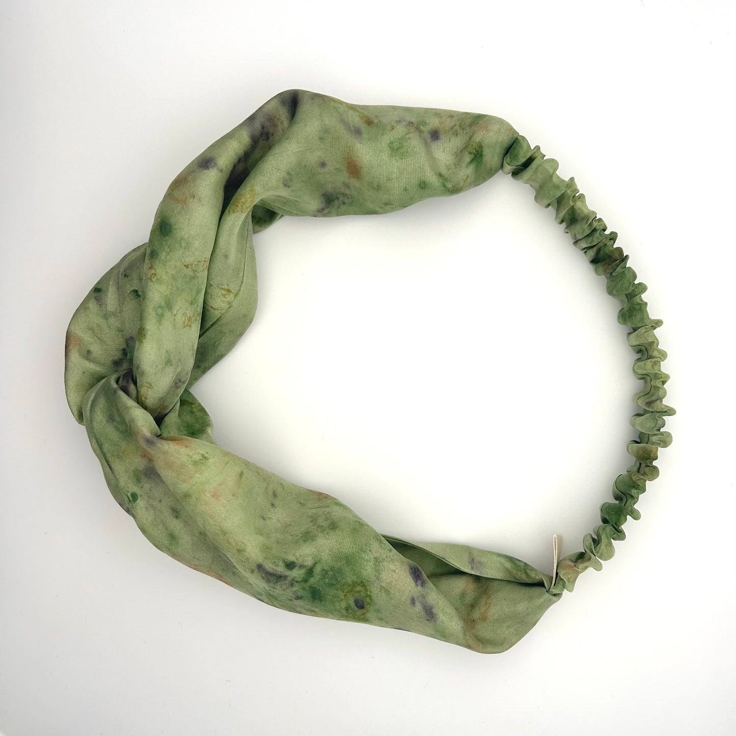 Green silk turban headband with elastic to secure over head which has been naturally dyed with purple pansy flowers
