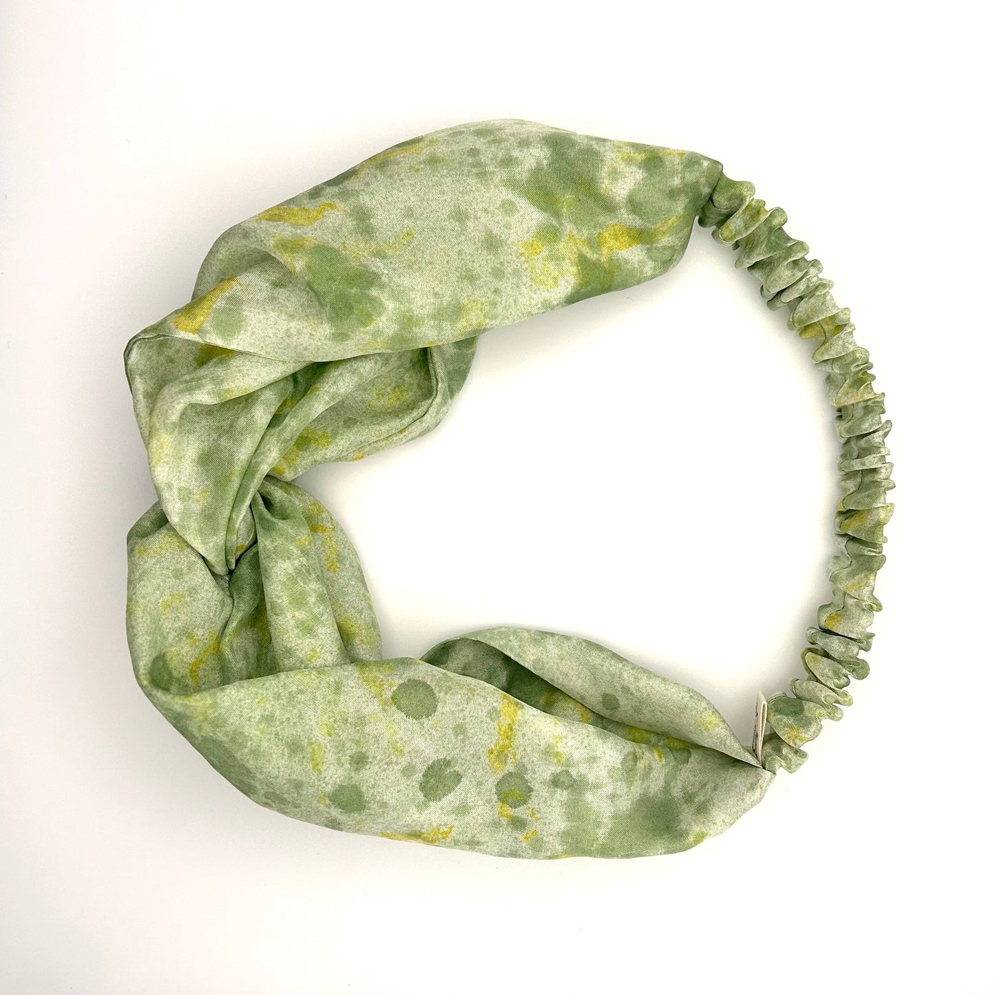 Green silk turban headband with elastic to secure over head which has been naturally dyed with yellow marigolds flowers and sprayed green pattern