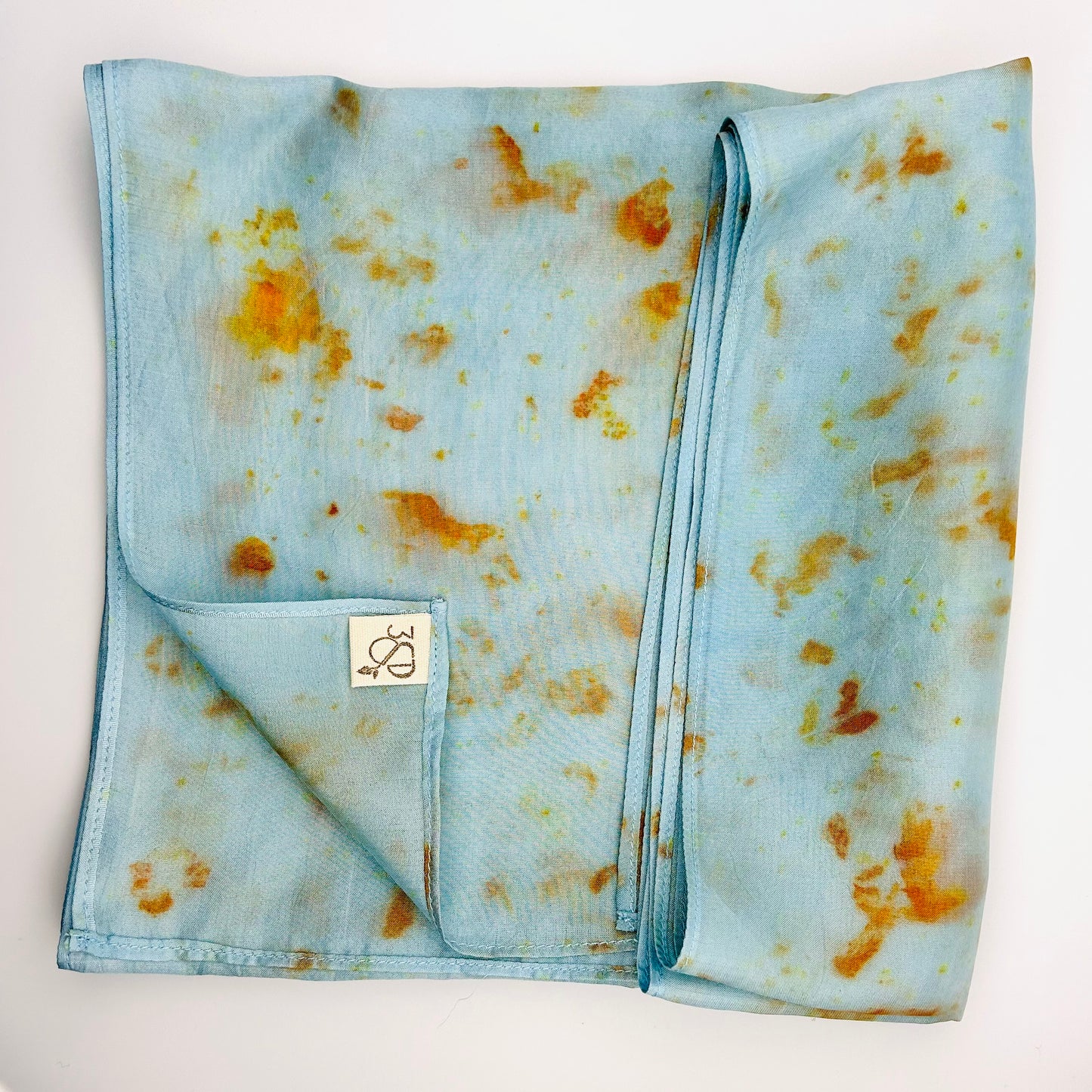 Pale indigo long silk scarf with naturally dyed hand-painted orange cosmos print showing scarf folded into a square