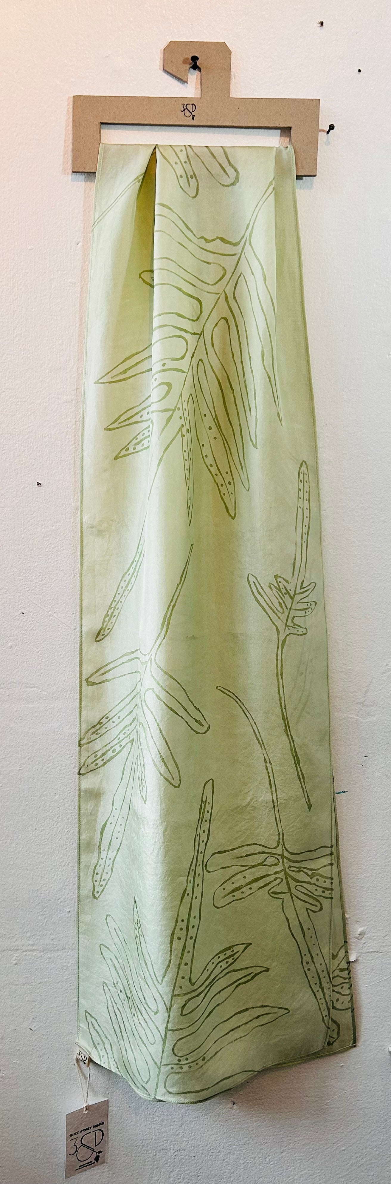 Pale green long silk scarf with naturally dyed hand-painted leaf print displayed on hanger showing half the length