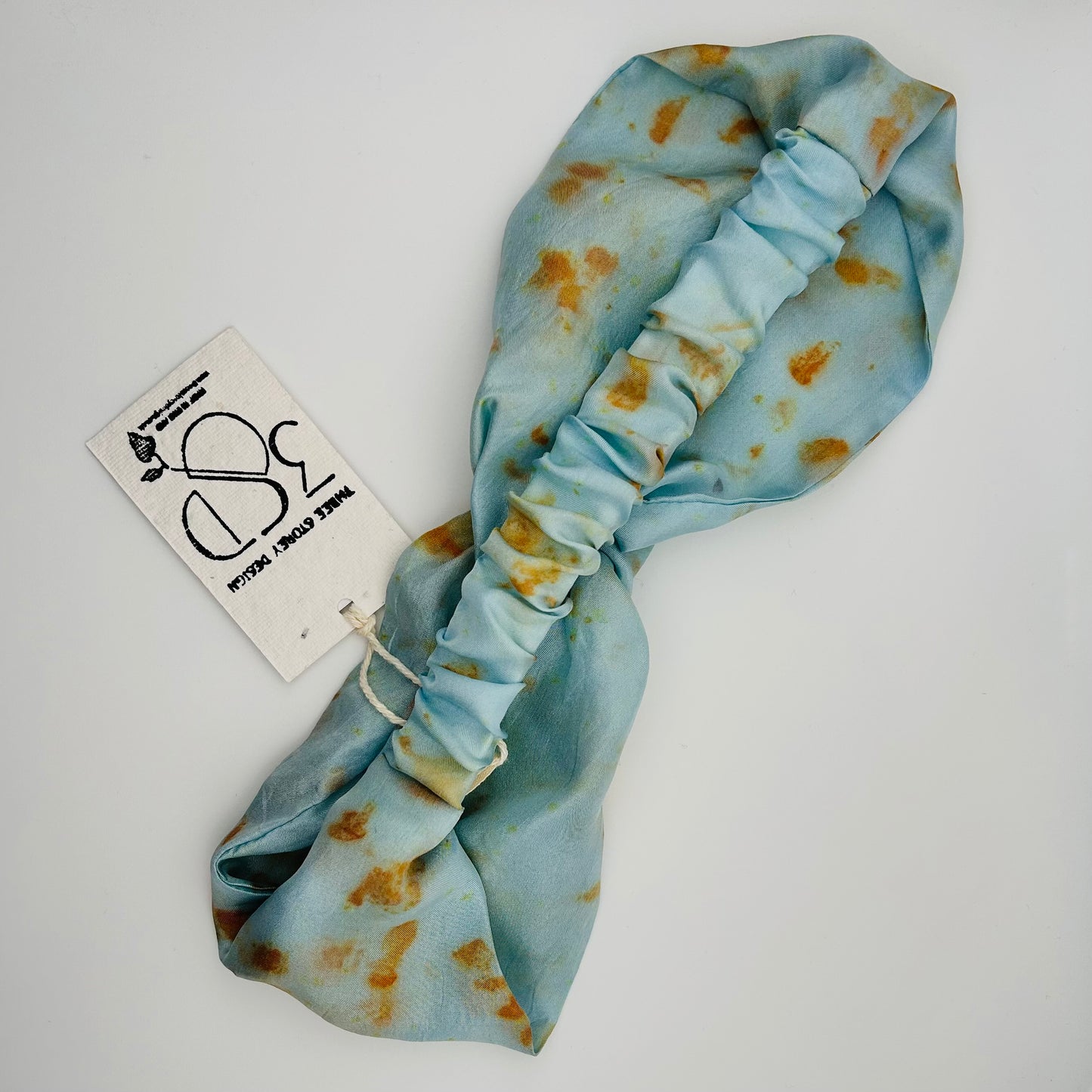 Back view of a Pale indigo silk turban headband with elastic to secure over head which has been naturally dyed with orange cosmos flowers