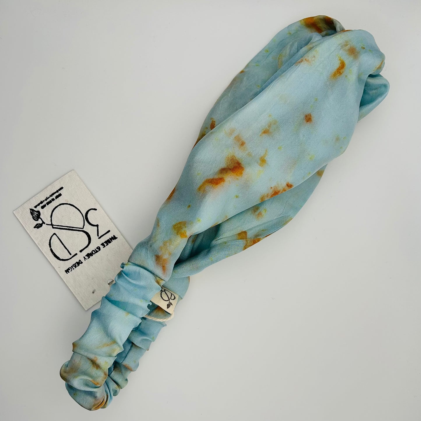 Side view of a Pale indigo silk turban headband with elastic to secure over head which has been naturally dyed with orange cosmos flowers