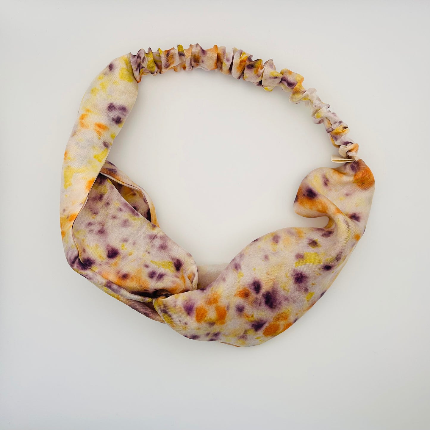 White silk turban headband with elastic to secure over head which has been naturally dyed with orange cosmos , black knight scabious and yellow marigold flowers