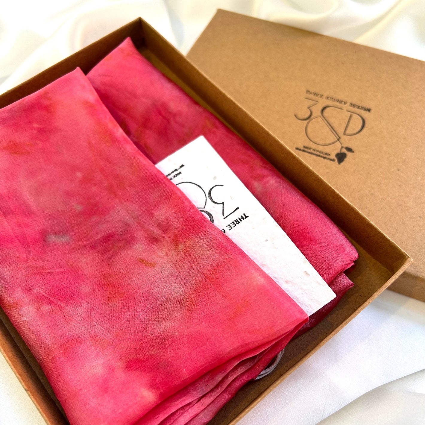 Bright pink cochineal naturally dyed  silk square scarf  folded into a square and displayed in a slim brown cardboard box