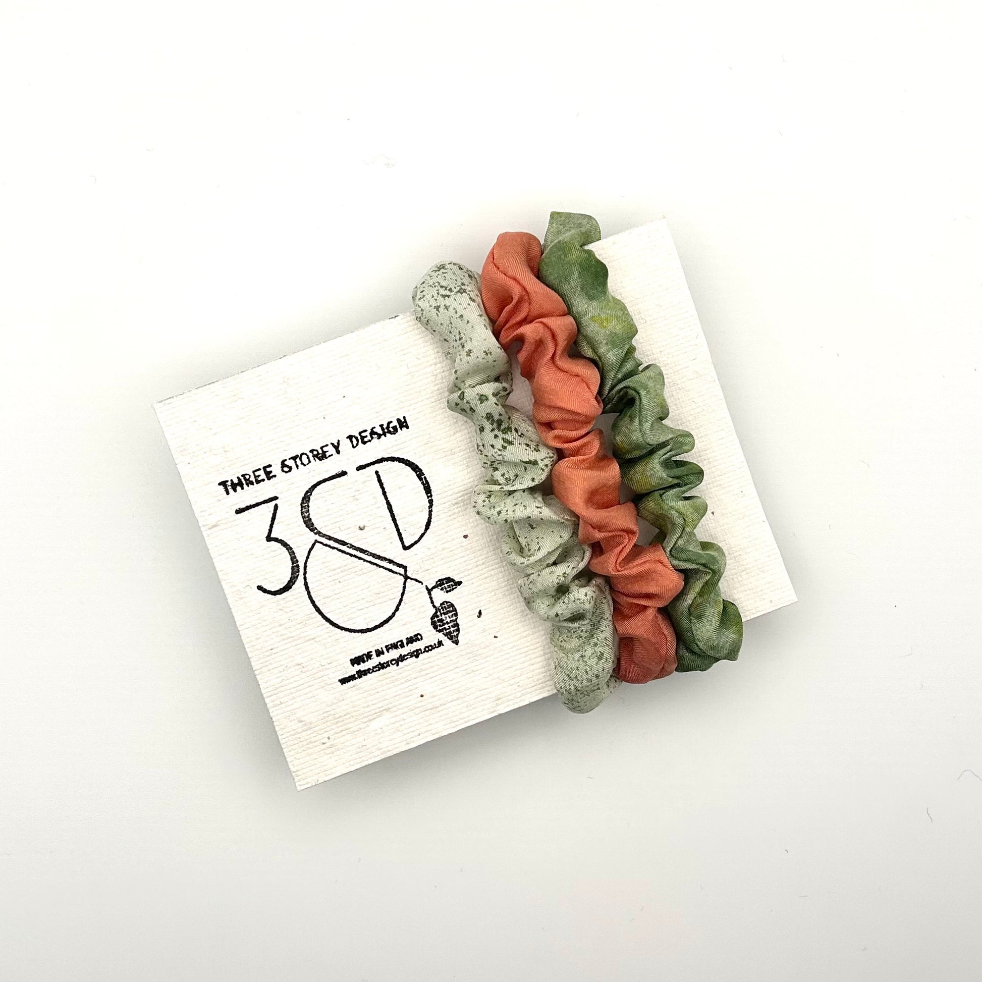 Pale green, Peach and Green naturally dyed 3 pack mini silk scrunchies presented on plantable branded packaging
