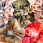 5 silk scrunchies with various naturally dyed prints of green, white, black bean, indigo, orange cosmos, bright pink