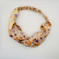 White silk turban headband with elastic to secure over head which has been naturally dyed with orange cosmos , black knight scabious and yellow marigold flowers 